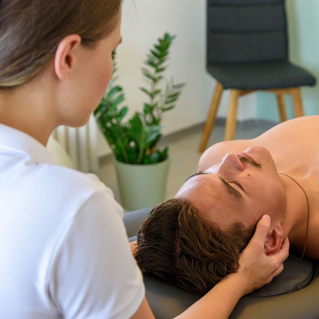 Therapeutin behandelt den Kopf eines liegenden Patienten